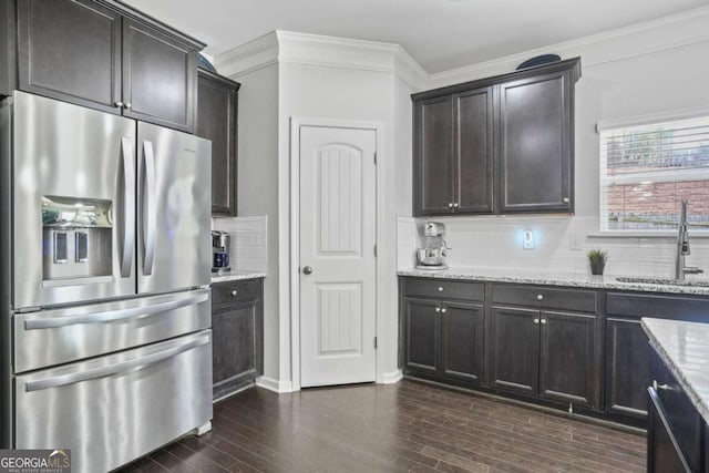 kitchen featuring light stone counters, a sink, stainless steel fridge, ornamental molding, and dark wood-style floors