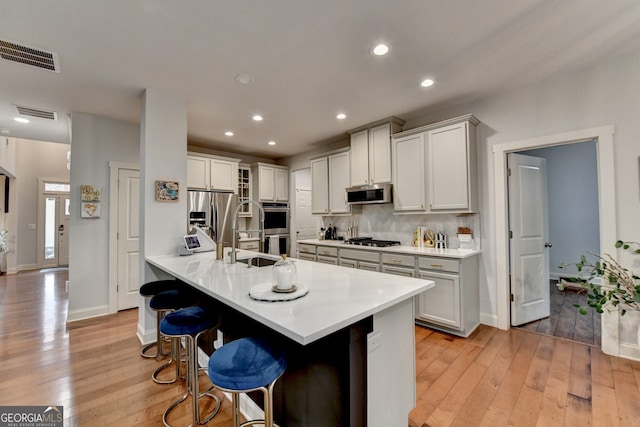 kitchen with kitchen peninsula, a kitchen breakfast bar, backsplash, stainless steel appliances, and light hardwood / wood-style flooring