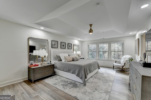 bedroom with ceiling fan, light wood-type flooring, and a tray ceiling