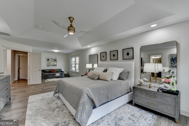 bedroom featuring ceiling fan, a raised ceiling, and wood-type flooring