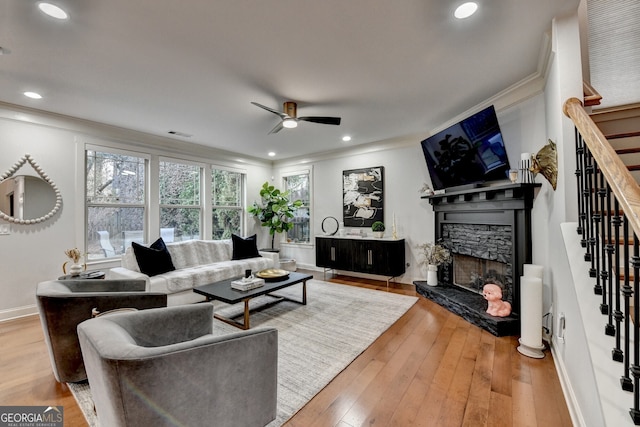 living room with a fireplace, light wood-type flooring, ceiling fan, and crown molding