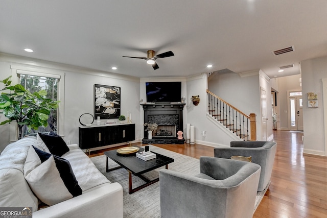 living room with hardwood / wood-style floors, a stone fireplace, ceiling fan, and crown molding