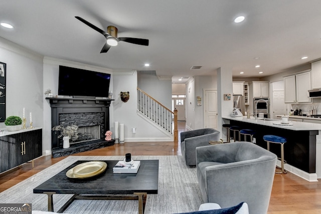 living room featuring ceiling fan, sink, light hardwood / wood-style floors, a fireplace, and ornamental molding