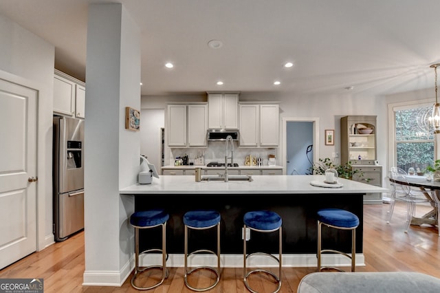 kitchen with pendant lighting, white cabinets, decorative backsplash, light wood-type flooring, and appliances with stainless steel finishes