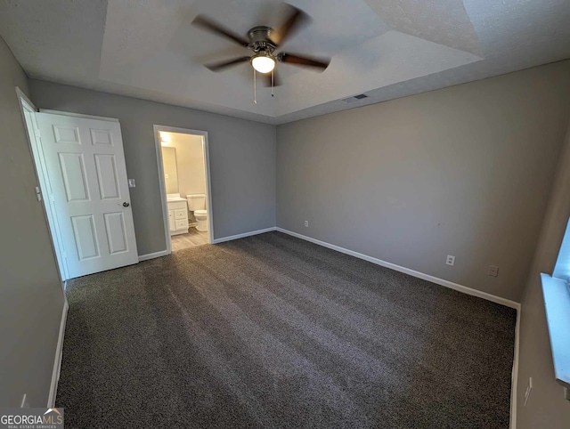 unfurnished bedroom featuring carpet, ceiling fan, ensuite bathroom, and a tray ceiling