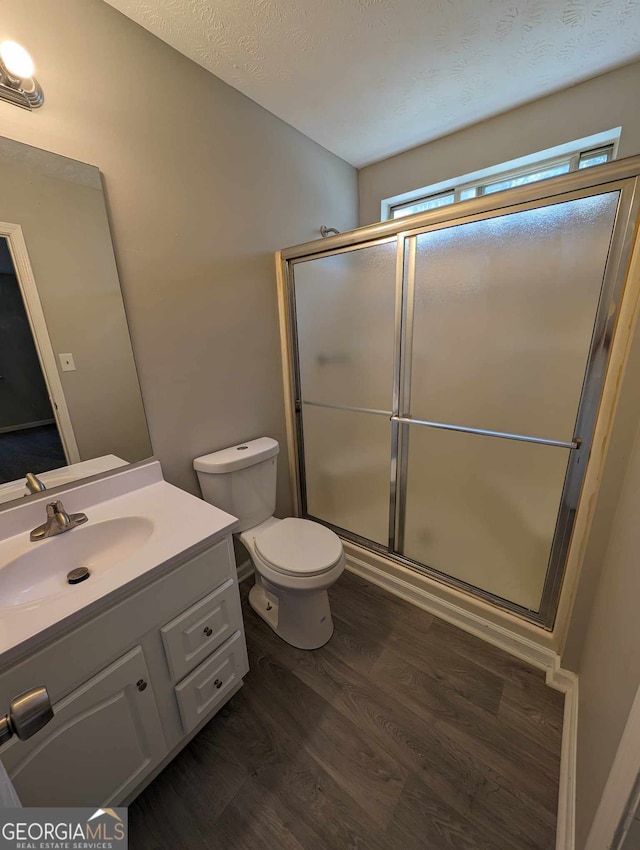 bathroom with hardwood / wood-style floors, vanity, a shower with door, toilet, and a textured ceiling