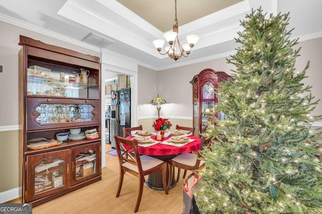 dining room featuring a tray ceiling, an inviting chandelier, light wood-type flooring, and ornamental molding