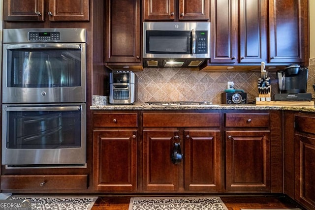 kitchen featuring tasteful backsplash, dark brown cabinetry, light stone countertops, and appliances with stainless steel finishes