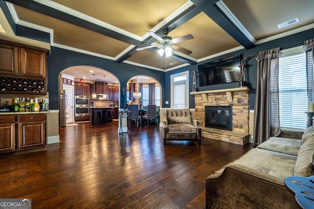 living room featuring coffered ceiling, a stone fireplace, ceiling fan, beamed ceiling, and dark hardwood / wood-style flooring