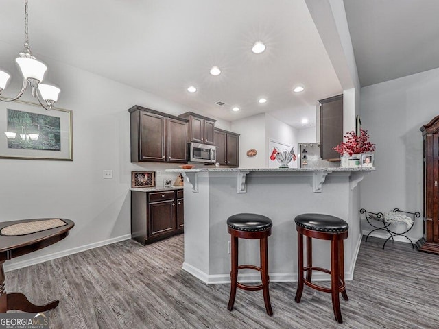 kitchen featuring dark brown cabinetry, light stone countertops, a kitchen breakfast bar, kitchen peninsula, and light wood-type flooring