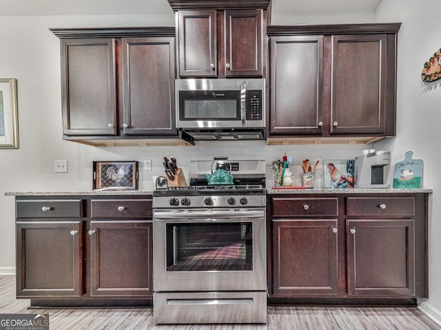 kitchen featuring light stone counters, dark brown cabinets, stainless steel appliances, and light hardwood / wood-style floors