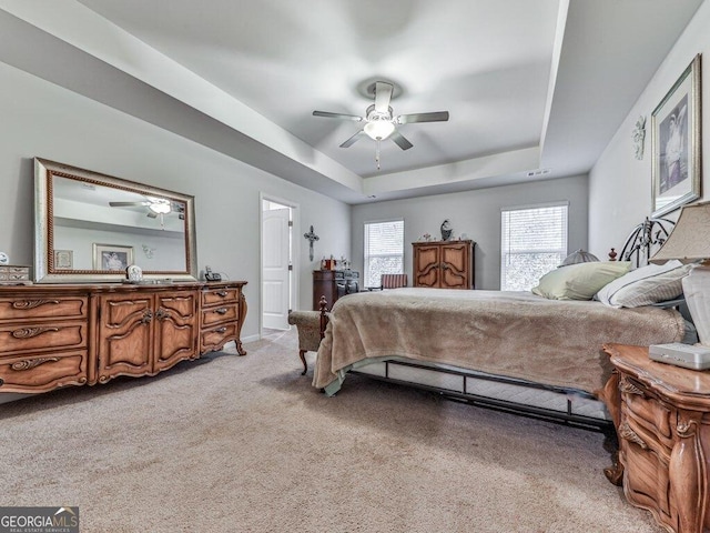 bedroom featuring light carpet, a tray ceiling, and ceiling fan