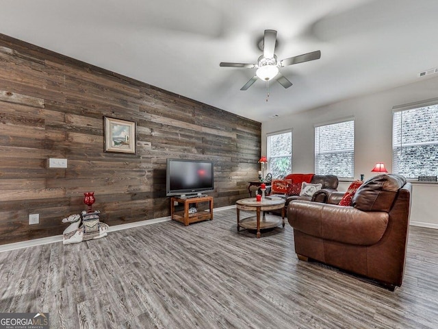 living room with hardwood / wood-style flooring, ceiling fan, and wooden walls