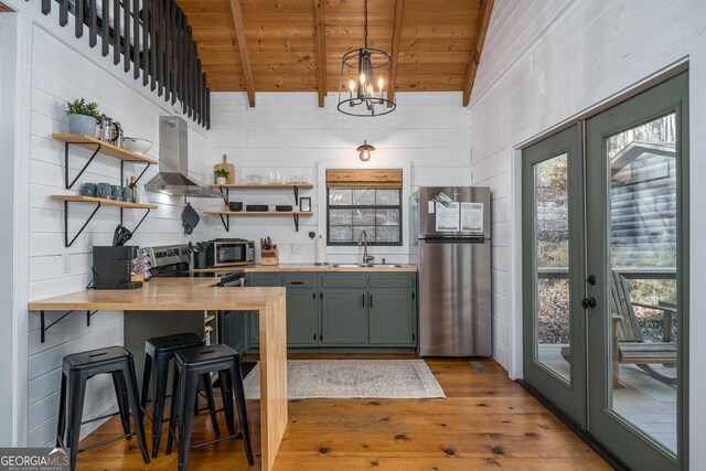 kitchen with appliances with stainless steel finishes, butcher block countertops, green cabinetry, and wall chimney range hood