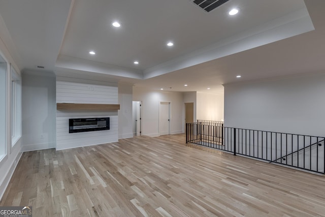 unfurnished living room with light wood-type flooring, a large fireplace, and a tray ceiling