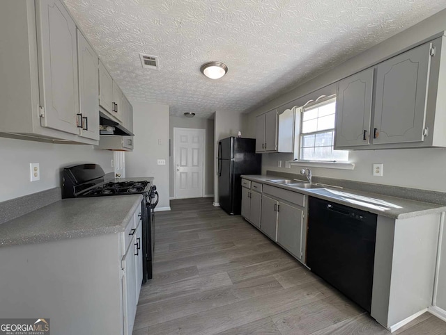 kitchen with black appliances, light hardwood / wood-style floors, sink, and a textured ceiling