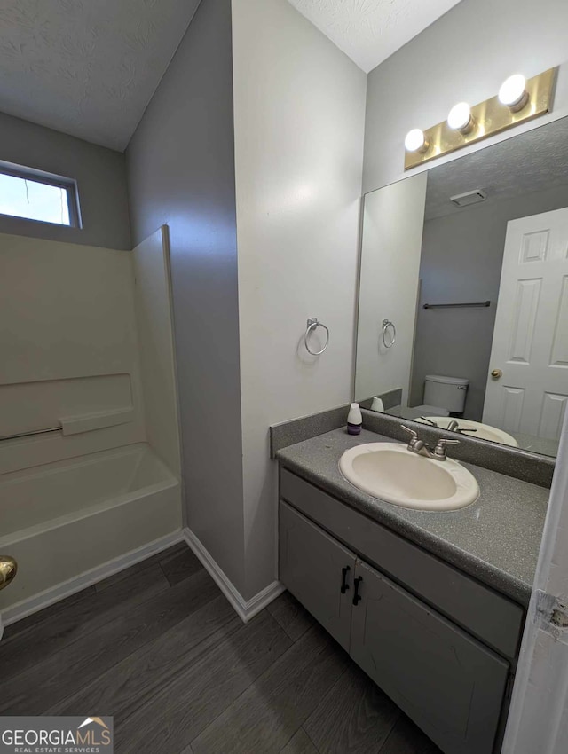 full bathroom featuring vanity, wood-type flooring, toilet, a textured ceiling, and shower / bath combination