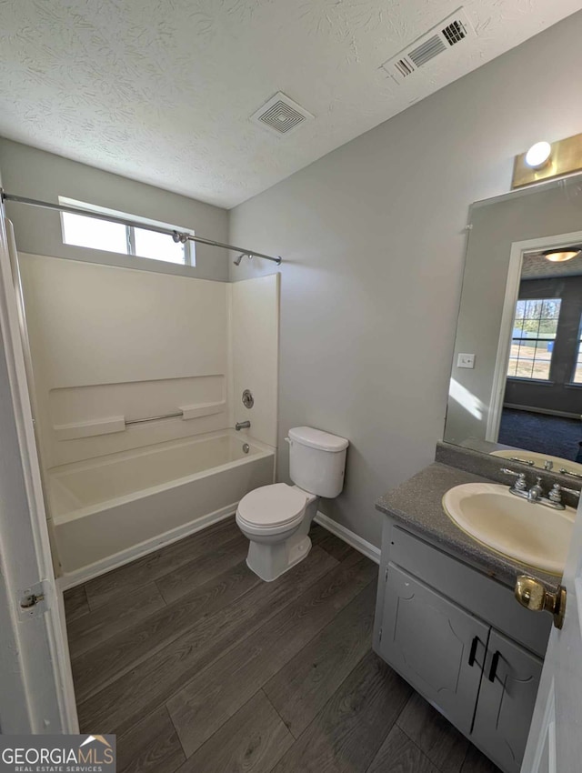 full bathroom with hardwood / wood-style floors, vanity,  shower combination, toilet, and a textured ceiling