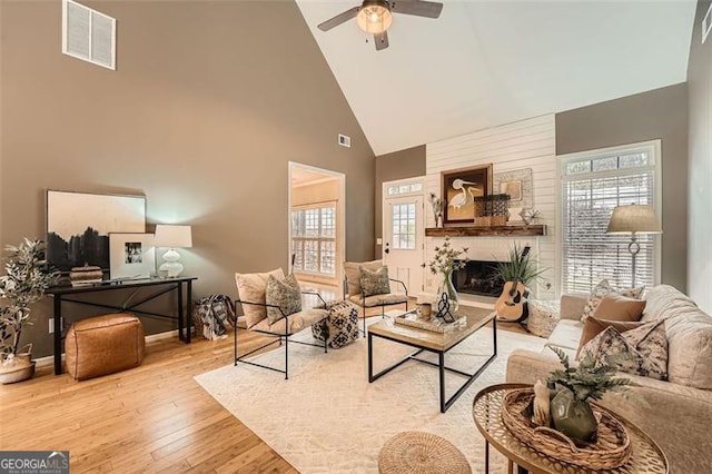 living room with a large fireplace, ceiling fan, light hardwood / wood-style floors, and high vaulted ceiling