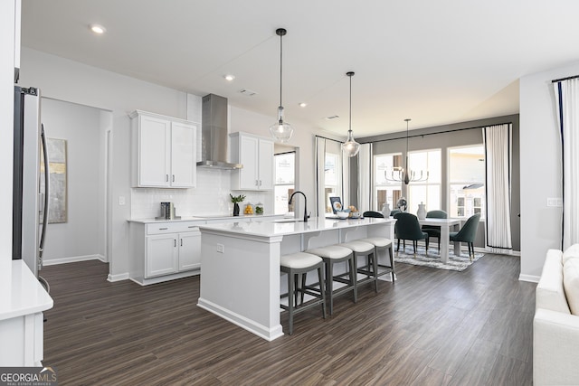 kitchen with a center island with sink, white cabinets, dark wood-type flooring, and wall chimney range hood