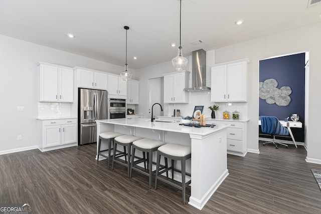 kitchen with stainless steel fridge, a kitchen island with sink, wall chimney range hood, pendant lighting, and white cabinets