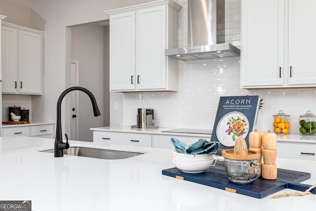 kitchen featuring white cabinets, backsplash, wall chimney range hood, and sink