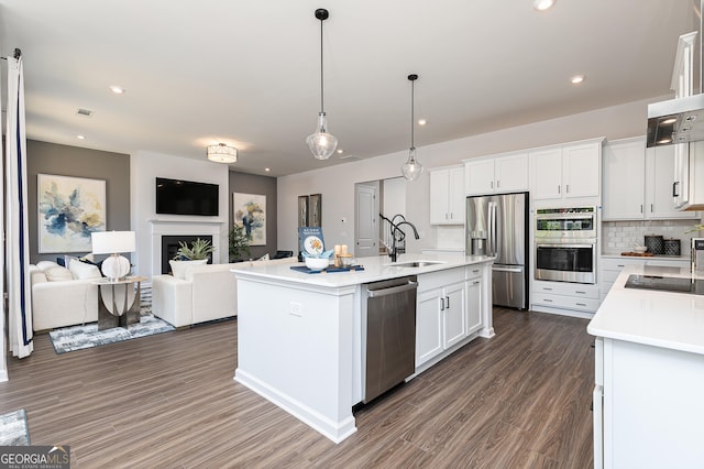 kitchen featuring stainless steel appliances, sink, decorative light fixtures, a center island with sink, and white cabinetry