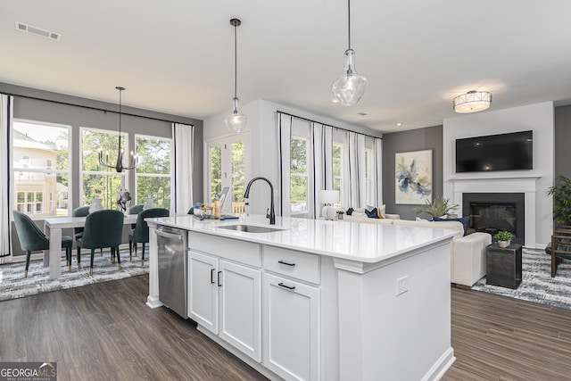 kitchen featuring a center island with sink, sink, hanging light fixtures, stainless steel dishwasher, and white cabinetry