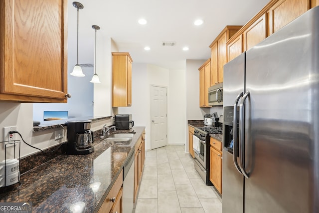 kitchen with stainless steel appliances, sink, pendant lighting, dark stone countertops, and light tile patterned flooring