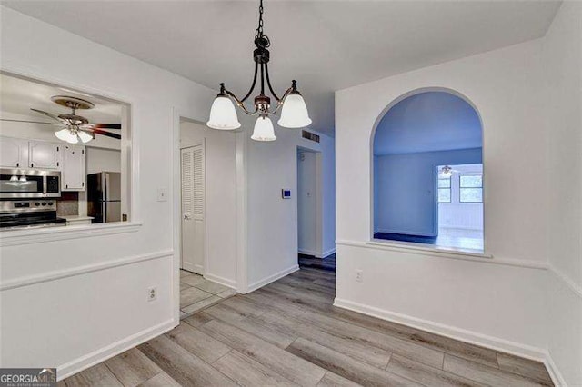 unfurnished dining area with ceiling fan with notable chandelier and light hardwood / wood-style floors