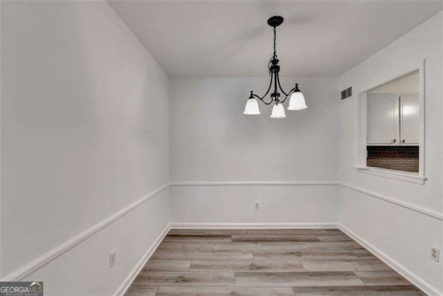 empty room with a notable chandelier and light hardwood / wood-style flooring