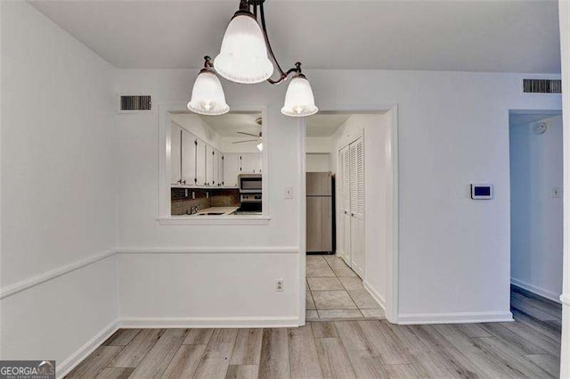 kitchen featuring decorative light fixtures, light wood-type flooring, stainless steel appliances, and white cabinetry