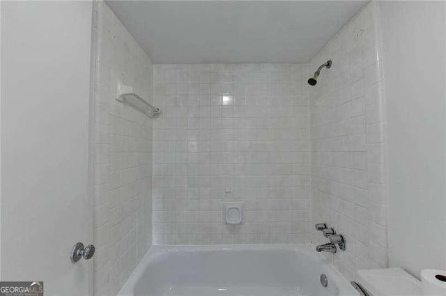 bathroom with tiled shower / bath combo and toilet