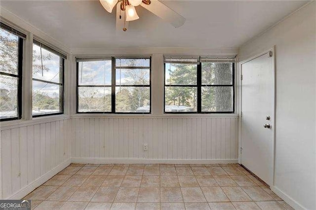 empty room with ceiling fan, plenty of natural light, and wood walls