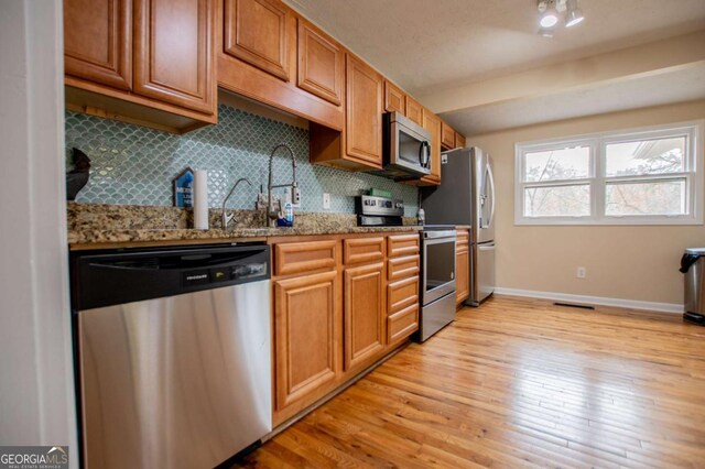 kitchen featuring light stone countertops, stainless steel appliances, light hardwood / wood-style flooring, and tasteful backsplash