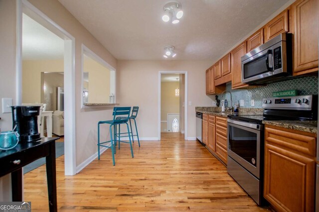 kitchen featuring dark stone counters, decorative backsplash, light hardwood / wood-style flooring, and stainless steel appliances