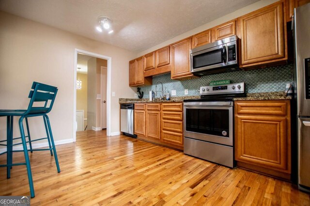 kitchen with stone countertops, light wood-type flooring, backsplash, and appliances with stainless steel finishes