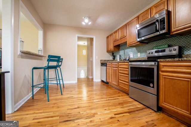 kitchen featuring tasteful backsplash, dark stone countertops, appliances with stainless steel finishes, and light hardwood / wood-style flooring