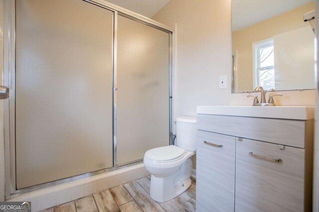 bathroom featuring a shower with shower door, toilet, wood-type flooring, and vanity