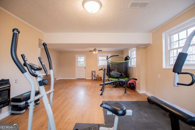 exercise room featuring ceiling fan, ornamental molding, a textured ceiling, and hardwood / wood-style flooring