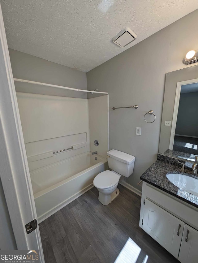 full bathroom with hardwood / wood-style floors, vanity, shower / washtub combination, toilet, and a textured ceiling