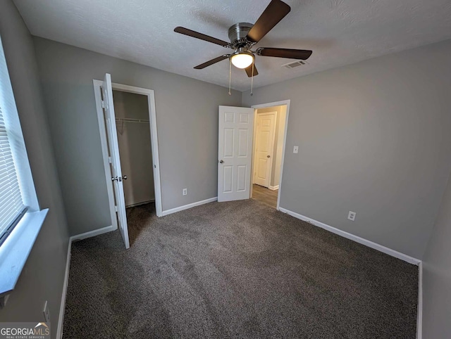 unfurnished bedroom with dark colored carpet, ceiling fan, a textured ceiling, and a closet