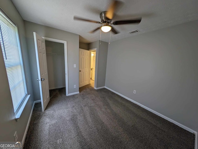 unfurnished bedroom featuring dark colored carpet, a textured ceiling, a closet, and ceiling fan