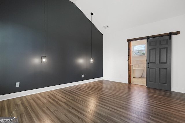 unfurnished room featuring a barn door, lofted ceiling, and dark wood-type flooring