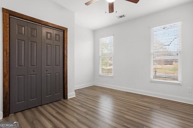 unfurnished bedroom with multiple windows, a closet, dark wood-type flooring, and ceiling fan