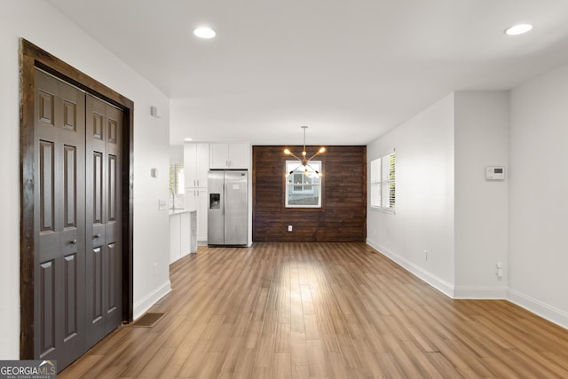 unfurnished living room with an inviting chandelier and light hardwood / wood-style flooring