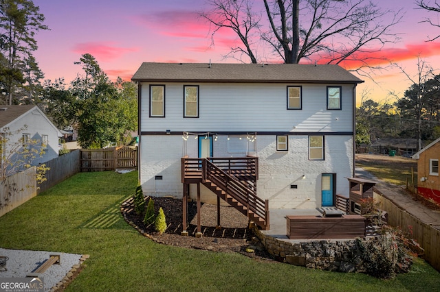 back house at dusk featuring a patio and a lawn