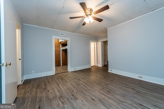 unfurnished bedroom with a walk in closet, dark hardwood / wood-style floors, ceiling fan, ornamental molding, and a closet