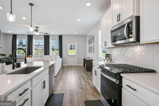 kitchen with a wealth of natural light, sink, stainless steel appliances, white cabinets, and light wood-type flooring