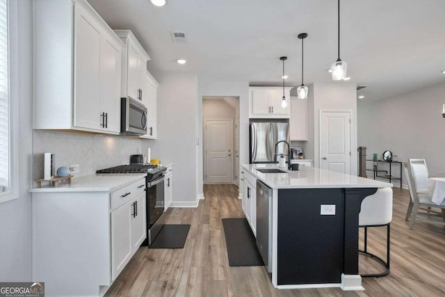 kitchen featuring white cabinetry, hanging light fixtures, stainless steel appliances, light hardwood / wood-style floors, and a kitchen island with sink